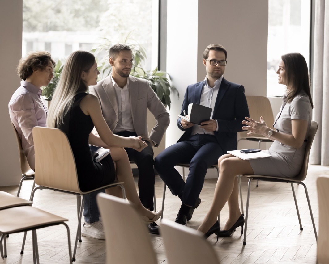 Cinco pessoas sentadas em cadeiras, em circulo, a falarem.